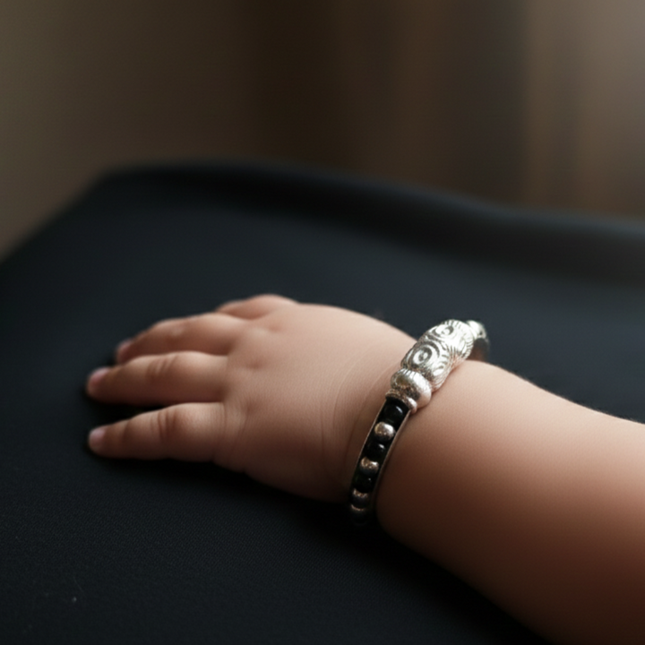 Ornate silver-toned baby kada bracelet with black bead accents.